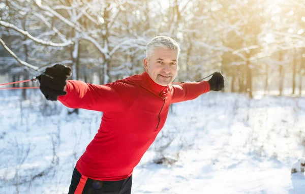 Hombre mayor activo haciendo ejercicio con banda de resistencia en el bosque nevado, espacio de copia. Concepto de pasatiempos al aire libre estacional —  Fotos de Stock