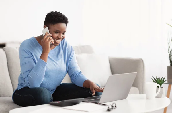 Jovem mulher negra falando no smartphone usando laptop — Fotografia de Stock