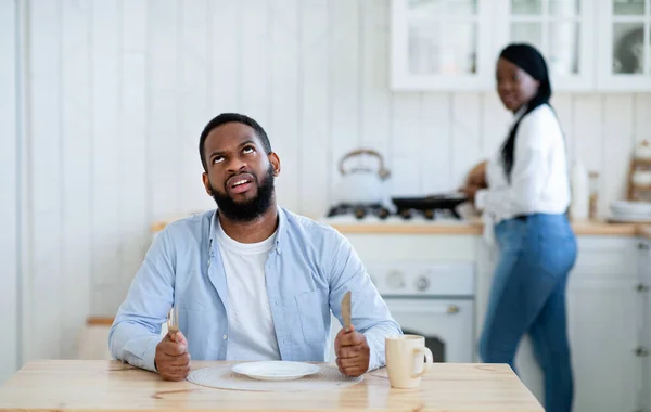 Ανυπόμονος πεινασμένος μαύρος σύζυγος περιμένει για δείπνο με άδειο πιάτο, δείχνοντας βαριεστημένος — Φωτογραφία Αρχείου