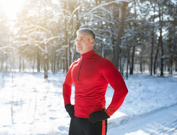 Feliz hombre mayor en ropa deportiva caliente tomando un descanso después de trotar en el bosque de invierno nevado. Actividades fuera de temporada —  Fotos de Stock