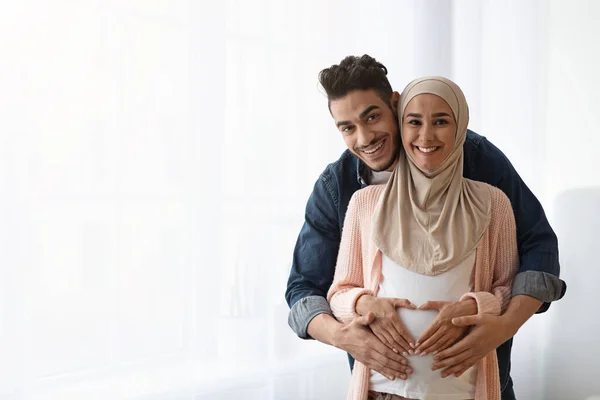 Retrato de feliz pareja musulmana embarazada posando cerca de la ventana en casa — Foto de Stock
