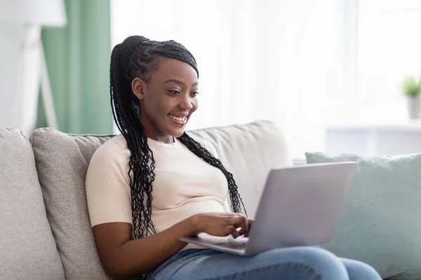 Χαρούμενη μαύρη γυναίκα ελεύθερη επαγγελματίας που εργάζεται από το σπίτι, χρησιμοποιώντας σύγχρονο φορητό υπολογιστή — Φωτογραφία Αρχείου