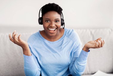 Siyah kadın oturuyor, kamerayla konuşuyor, kulaklık takıyor.