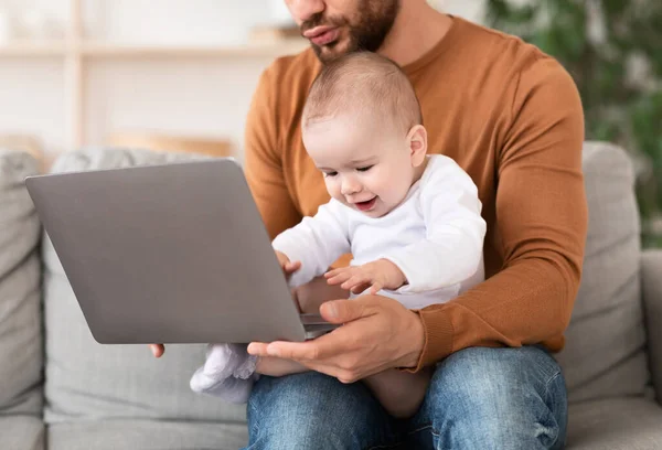 Pai usando laptop sentado com bebê de joelhos em casa — Fotografia de Stock