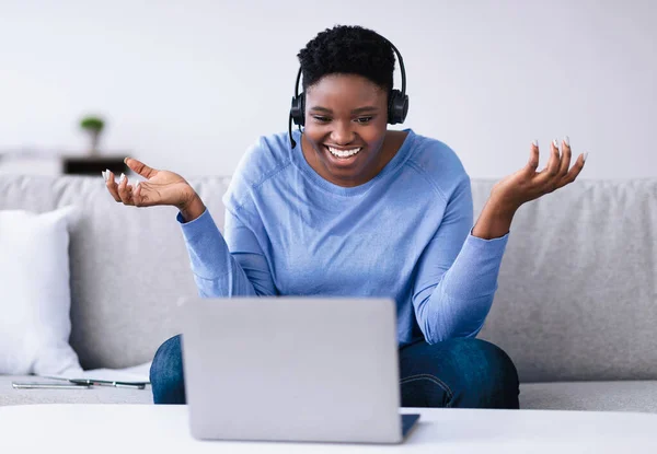 Siyahi kadın kanepede oturuyor, bilgisayarında video görüşmesi yapıyor. — Stok fotoğraf