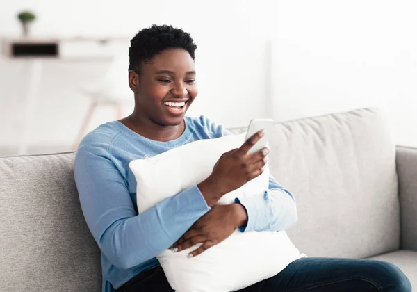 Sorrindo mulher negra usando telefone celular, segurando travesseiro — Fotografia de Stock