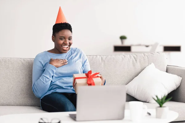 Şapkalı Afrikalı Amerikalı Kadın Dizüstü bilgisayar kullanarak hediye kutusunu tutuyor — Stok fotoğraf