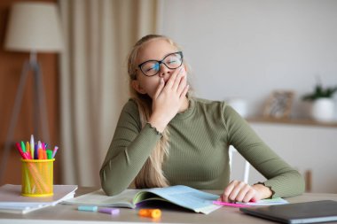 Uykulu genç kız evde ödev yapıyor.