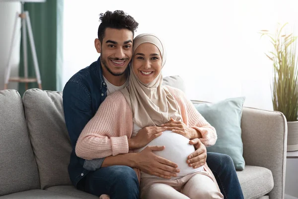 Feliz pareja musulmana religiosa esperando un bebé posando en el sofá en casa — Foto de Stock