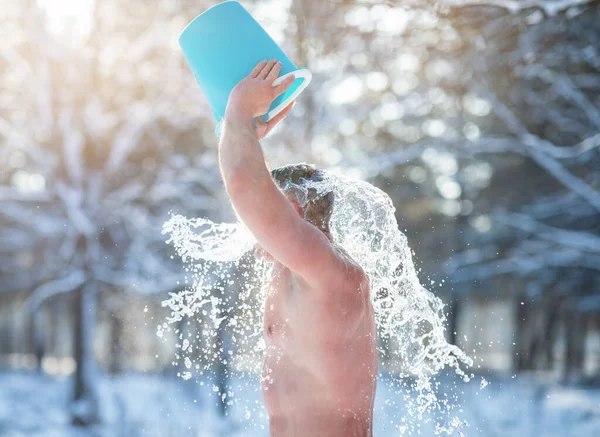 Reifer Mann schüttet sich im verschneiten Winterwald eisiges Wasser aus einem Eimer auf den Kopf. Entwicklung von Kälteresistenz — Stockfoto