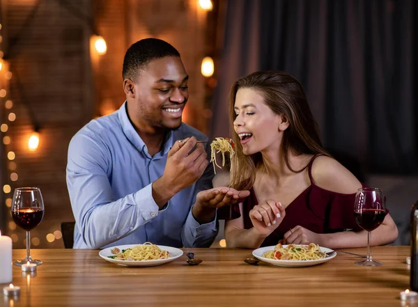 Casal Interracial romântico se divertindo durante o jantar no restaurante, comendo espaguete juntos — Fotografia de Stock
