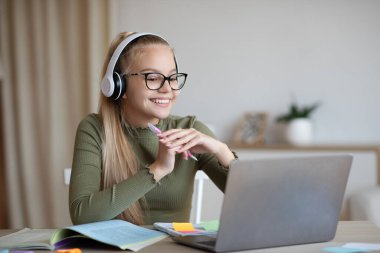 Sevimli genç kız bilgisayarını ve kulaklığını kullanarak uzaktan çalışmaktan zevk alıyor.