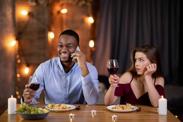 Скучное свидание. Черный парень разговаривает по телефону в ресторане, игнорирует свою девушку — стоковое фото