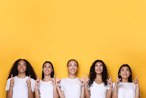 Pięć wielonarodowych kobiet wytykających palcami w górę pozowanie na żółtym tle — Zdjęcie stockowe