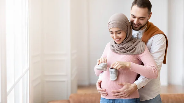 Moslim echtgenoot zetten kleine schoenen op zwangere vrouwen buik Indoor — Stockfoto