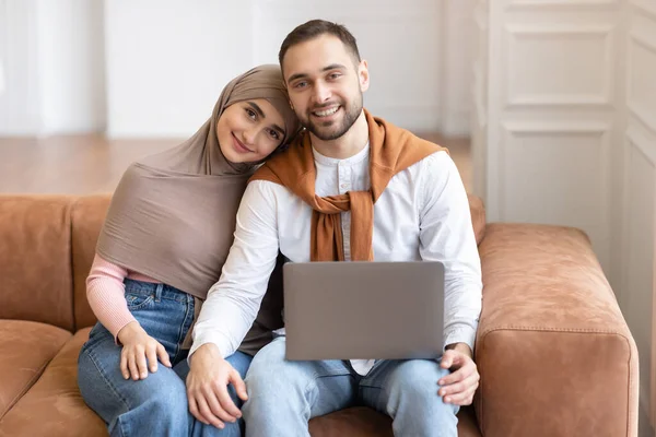 幸せなイスラム教徒のカップルは、自宅でノートパソコンの抱擁ポーズで座っています — ストック写真