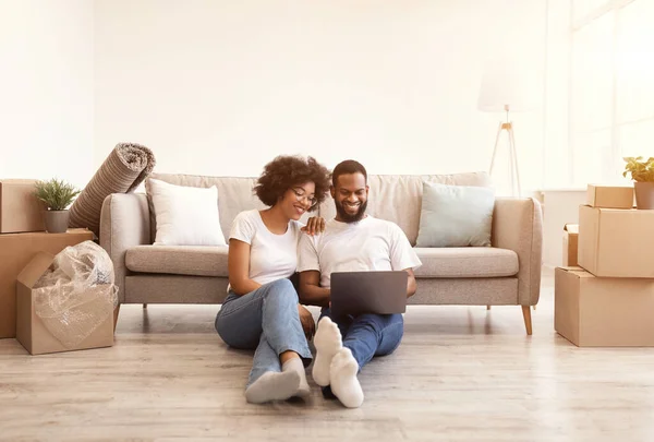 Černý pár pomocí notebooku sedí uvnitř po přestěhování nového domova — Stock fotografie