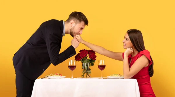 Chłopak całowanie dziewczyny ręka siedzi przy stole na żółtym tle — Zdjęcie stockowe