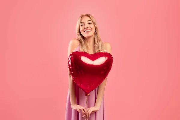 Milovníci prázdnin koncept. Sexy mladá dáma na sobě hezké šaty, drží červené srdce ve tvaru balónu na růžovém pozadí studia — Stock fotografie