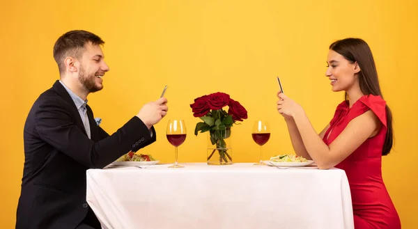Casal feliz usando smartphones durante o jantar romântico, fundo amarelo, Panorama — Fotografia de Stock