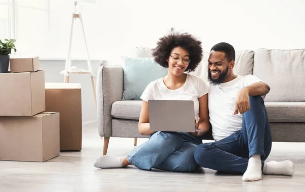 Casal preto usando laptop sentado entre as caixas móveis na casa — Fotografia de Stock