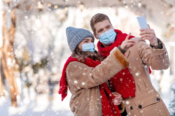 Paar mit Gesichtsmasken macht Winter-Selfie mit Smartphone — Stockfoto