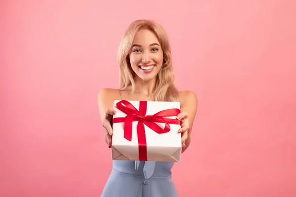 Bella giovane donna dando scatola regalo avvolto a macchina fotografica su sfondo rosa studio — Foto Stock