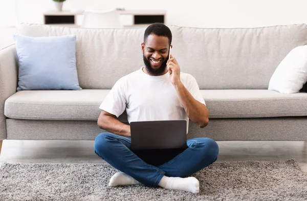 Hombre freelancer africano usando el ordenador portátil hablando por teléfono en casa —  Fotos de Stock