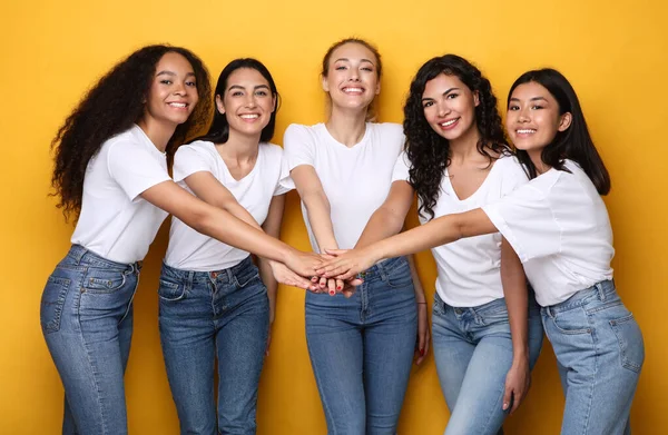 Cinque allegre donne diverse che tengono le mani in piedi su sfondo giallo — Foto Stock