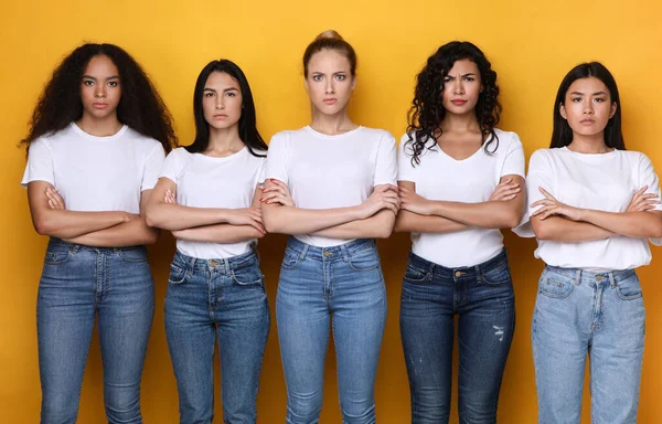 Cinco mujeres mixtas descontentas posando cruzando las manos sobre fondo amarillo — Foto de Stock