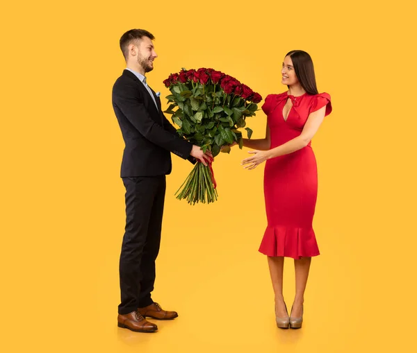 Chłopak dając dziewczynie bukiet czerwonych róż na żółtym tle — Zdjęcie stockowe
