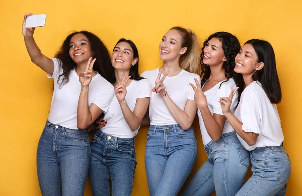 Grupp av kvinnor att göra selfie på mobiltelefon, gul bakgrund — Stockfoto