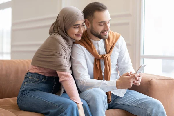 Вид сбоку мусульманской пары с помощью смартфона, сидя дома — стоковое фото