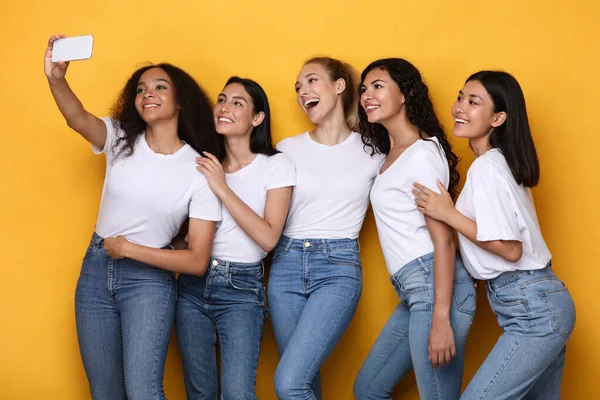 黄色の背景にスマートフォンでセルフィーを作る幸せな多人種間の女性 — ストック写真