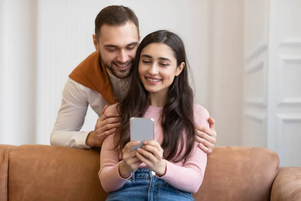 Moderna pareja árabe utilizando la aplicación de teléfono móvil sentado en casa —  Fotos de Stock