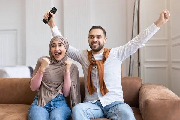 Radostný muslim pár sledování televize gestikulace Ano sedí doma — Stock fotografie