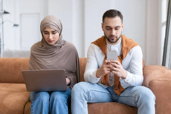 Cônjuges muçulmanos usando laptop e telefone móvel sentado em casa — Fotografia de Stock