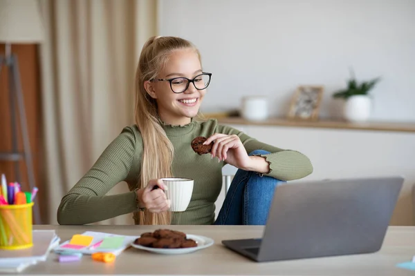 Positive teen girl drinking tea and watching movie online — Stock Photo, Image