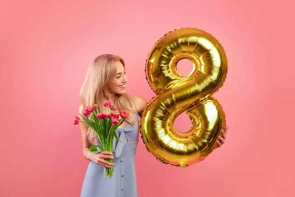 Sexy jeune femme avec des fleurs et ballon doré en forme de numéro huit sur fond de studio rose — Photo