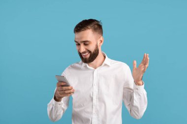 Gülümseyen sakallı adam akıllı telefon kullanıyor, internette sörf yapıyor, mavi stüdyo üzerinden iletişim kuruyor.