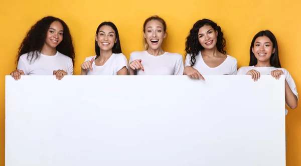 Donne multiculturali che tengono il bordo vuoto di carta sopra lo sfondo giallo, Mockup — Foto Stock