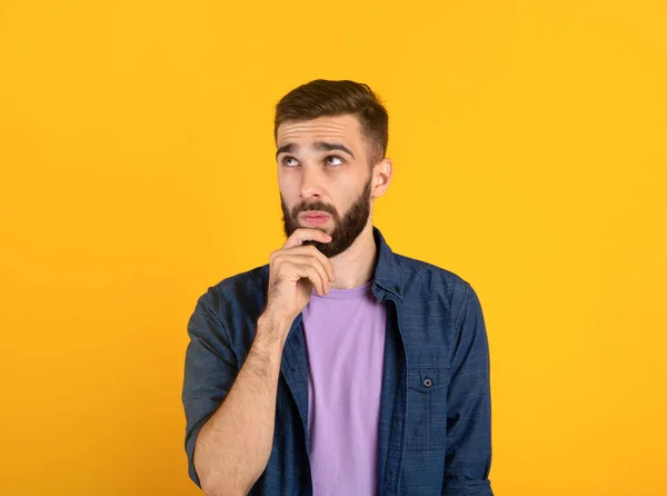 Düşünceli genç sakallı bir adamın portresi çenesine dokunuyor, turuncu stüdyo arka planında derin düşüncelere dalmış — Stok fotoğraf