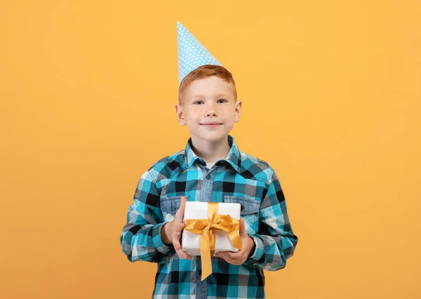 Sorrindo aniversário menino segurando presente, fundo amarelo — Fotografia de Stock