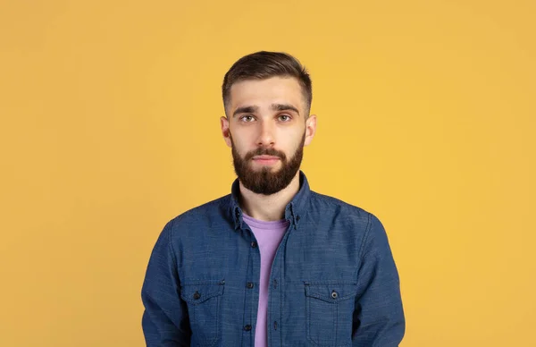 Sıradan giyinmiş karizmatik sakallı genç adamın portresi turuncu stüdyo arkaplanından kameraya bakıyor. — Stok fotoğraf