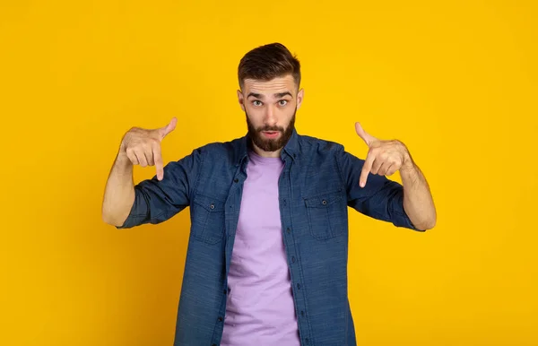 Tipo barbudo sorprendido apuntando hacia abajo sobre fondo de estudio naranja, panorama — Foto de Stock