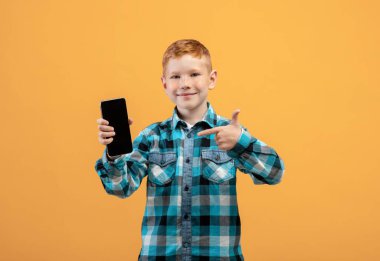 Gülümseyen çocuk boş ekranla cep telefonunu işaret ediyor.