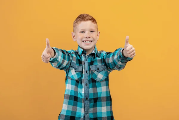 Szczęśliwy imbir dzieciak pokazując kciuki w górę na żółty studio tło — Zdjęcie stockowe