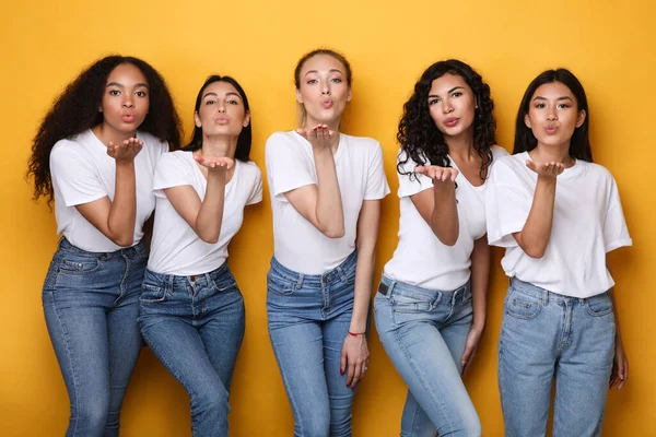 Cinco mulheres multiculturais felizes soprando beijos para câmera, fundo amarelo — Fotografia de Stock