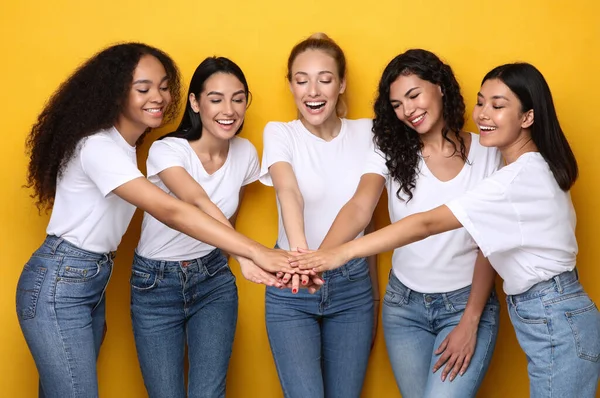 Об "єднані багаторасові жінки тримають руки, щоб бути разом, жовте тло — стокове фото