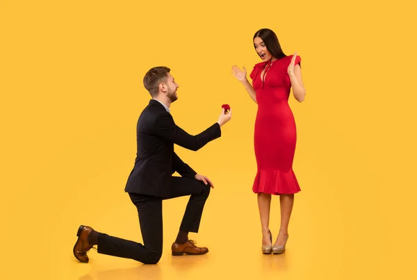 Мужчина предлагает девушке обручальное кольцо, стоящее на коленях, жёлтый фон — стоковое фото
